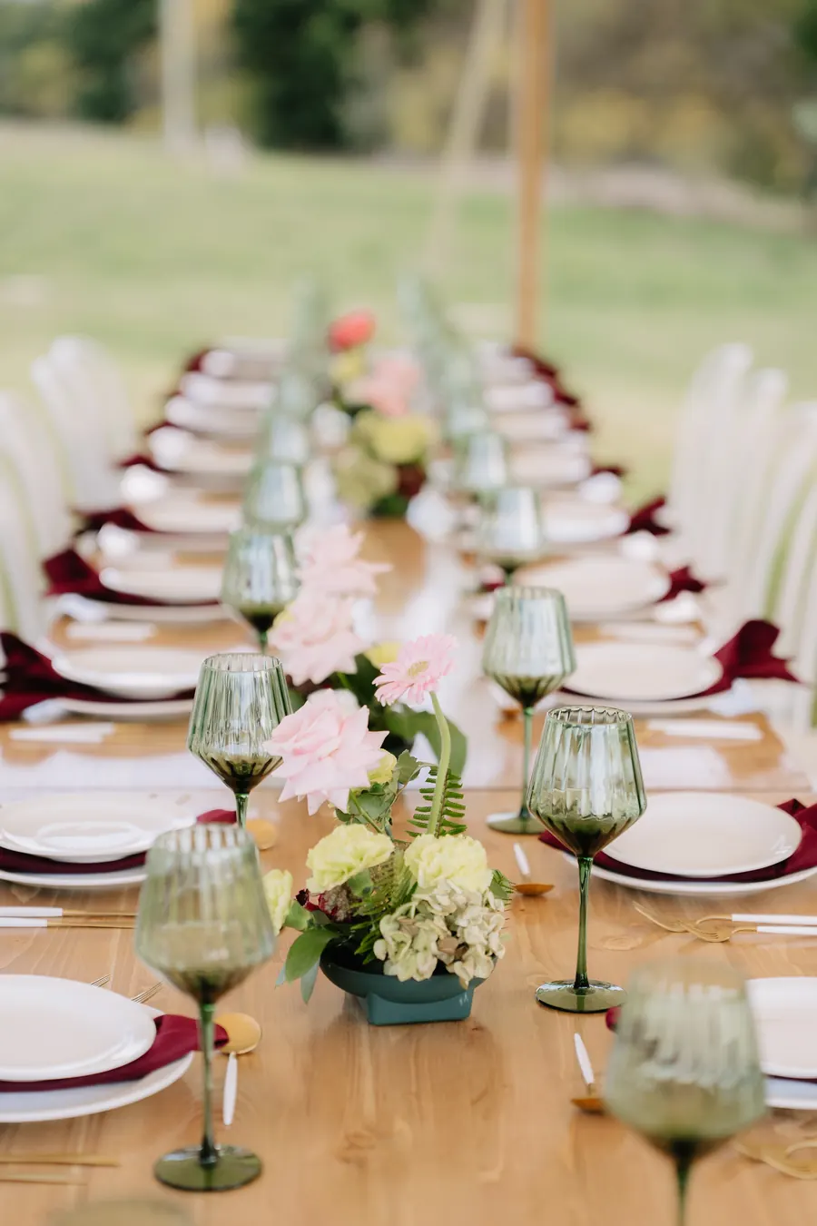 A long table set with glassware and flowers on a lawn