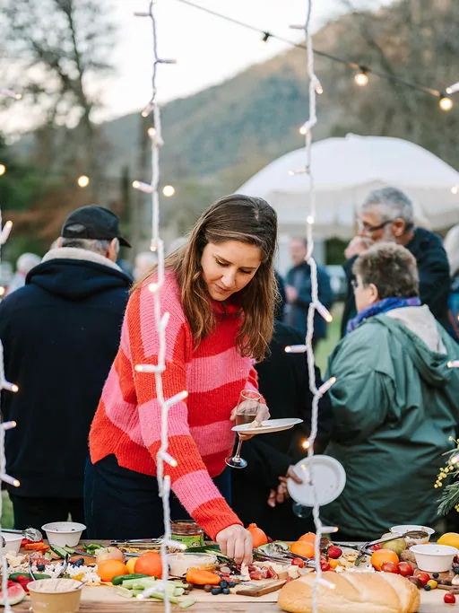 Guests around a long grazing table under festoon lights at dusk
