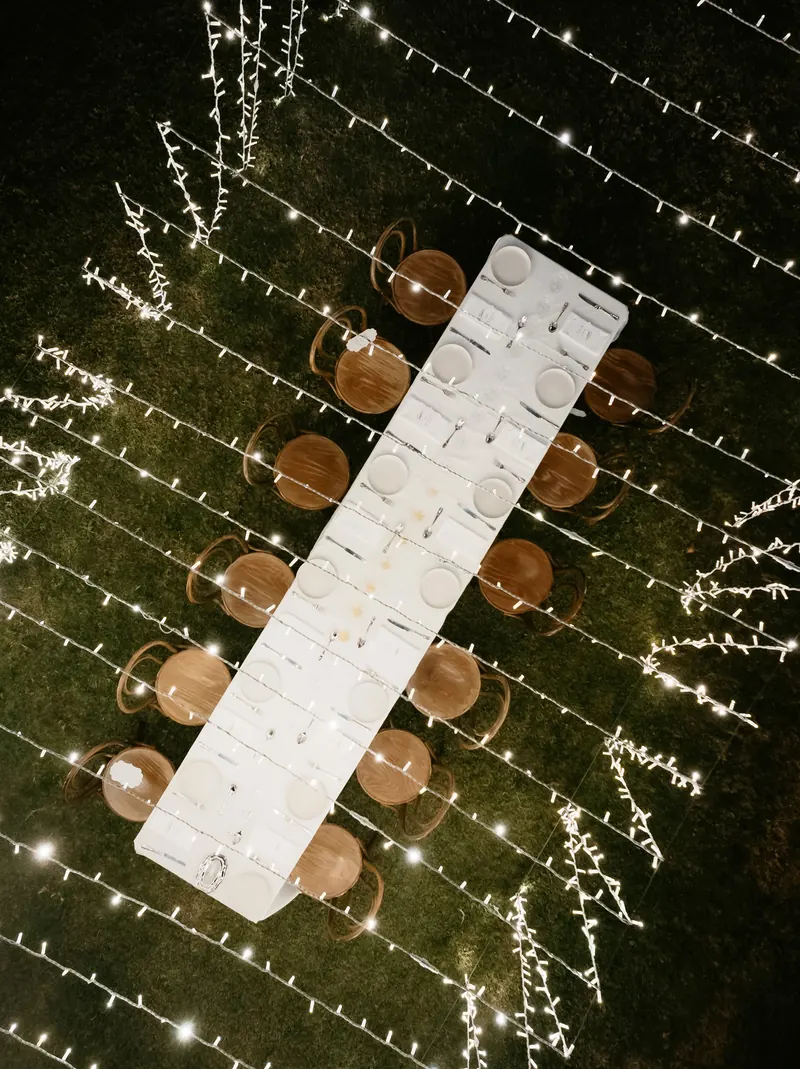 Long dinner table under criss-crossing fairy lights, from above