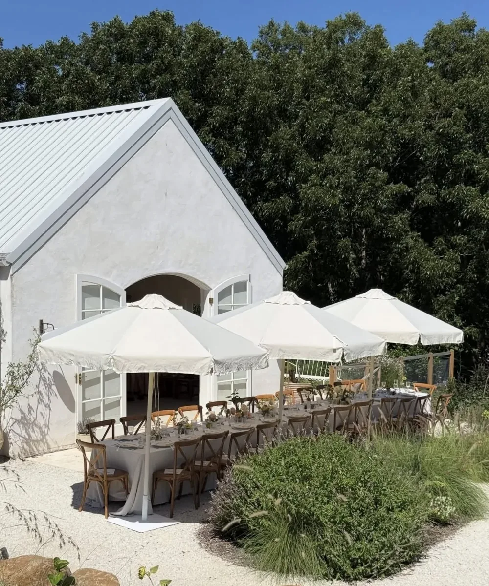 Outdoor lunch tables beneath umbrellas beside a garden venue